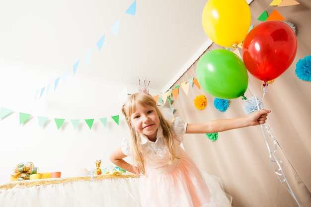 Klein feestvarken met kroon op het hoofd met kleurrijke ballonnen. de prinses op het verjaardagsfeestje