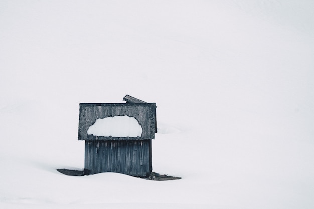 Gratis foto klein houten handgebouwd huis in een bos dat in sneeuw op een sneeuwheuvel wordt behandeld