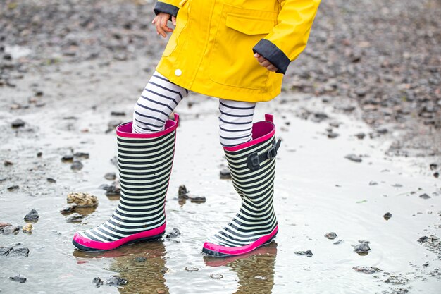 Klein kind in een felgele regenjas en gestreepte rubberen laarzen.