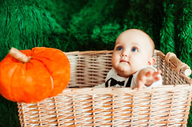 Klein kind met blauwe ogen zit in een mand met speelgoed pompoenen
