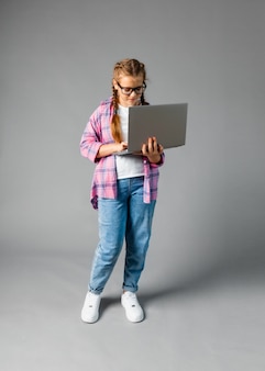 Klein meisje 12-13 jaar oud, met een laptop geïsoleerd op een grijze achtergrond. kopieer ruimte voor kopiëren.