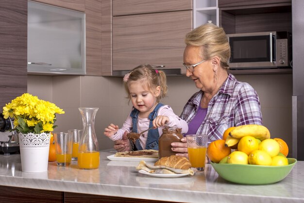 Klein meisje bereidt pannenkoeken met chocoladeroom in de keuken met haar grootmoeder