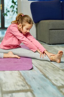 Klein meisje doet rekoefeningen, oefent thuis yoga op fitnessmat