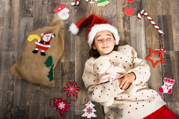 Klein meisje, gekleed in Santa Claus liggend op haar rug, omringd door kerstversiering en een zak