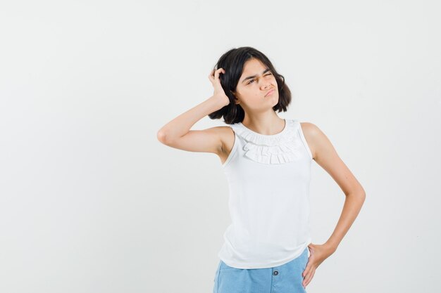 Klein meisje hand in hand in witte blouse, korte broek en besluiteloos op zoek. vooraanzicht.