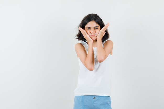 Klein meisje hand in hand op waait wangen in witte blouse, korte broek en op zoek schattig, vooraanzicht.