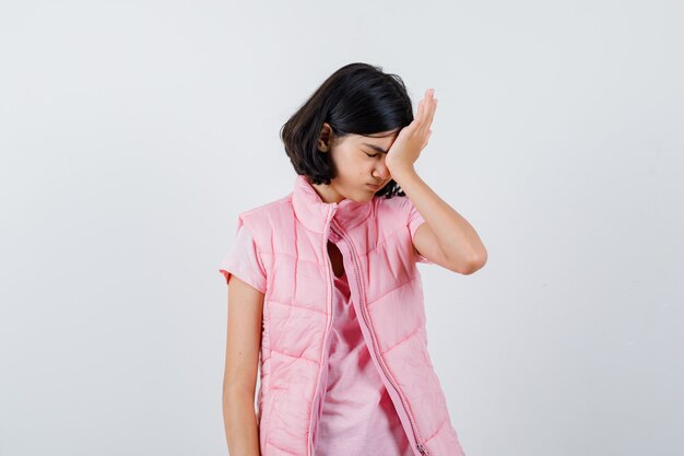 Klein meisje in een t-shirt en puffer vest met hand op voorhoofd