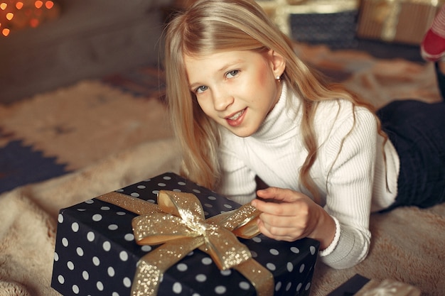 Klein meisje in een witte trui in de buurt van kerstboom met heden