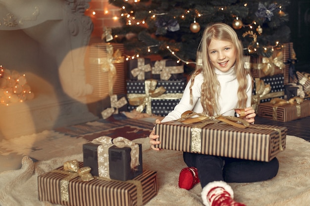 Klein meisje in een witte trui in de buurt van kerstboom met heden