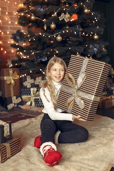 Klein meisje in een witte trui in de buurt van kerstboom met heden