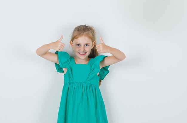 Klein meisje in groene jurk duimen opdagen en vrolijk kijken