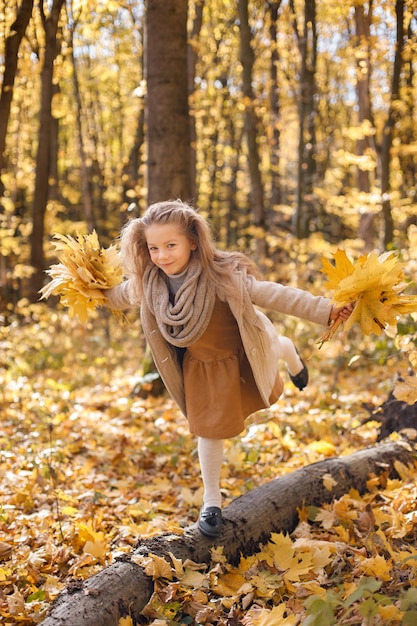 Klein meisje in mode kleding permanent in herfst bos. Meisje met een gele bladeren. Meisje draagt bruine jurk en een jas.