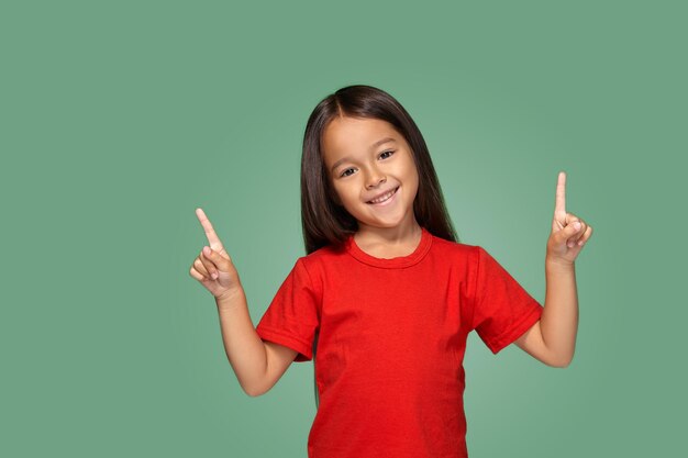 Klein meisje in rood t-shirt met vinger omhoog op een groene achtergrond