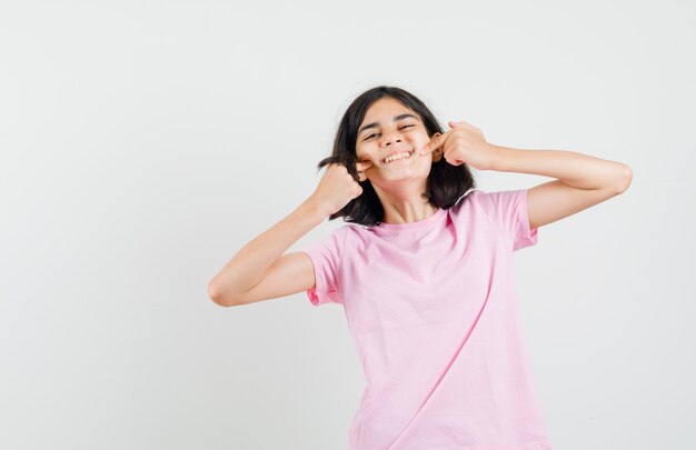 Klein meisje in roze t-shirt wijzend op haar kuiltjes en kijkt blij, vooraanzicht.