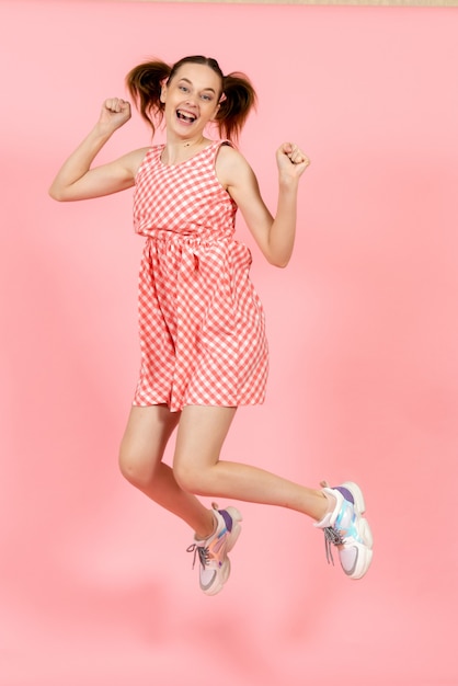 klein meisje in schattige lichte jurk gelukkig springen op roze