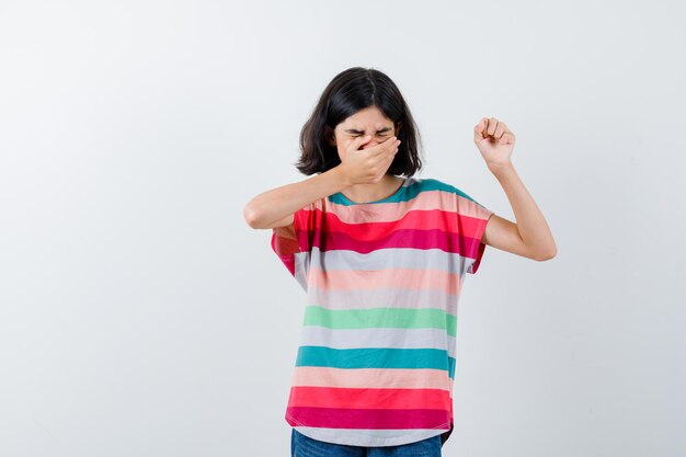 Klein meisje in t-shirt hand op mond houden, hand opsteken en walgen, vooraanzicht.