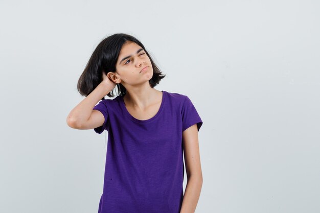 Klein meisje in t-shirt hoofd krabben en op zoek attent,