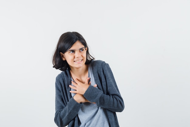 Klein meisje in t-shirt, jas hand in hand op de borst en op zoek vrolijk