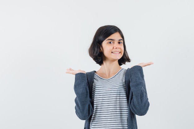 Klein meisje in t-shirt, jasje dat iets presenteert of vergelijkt en er zelfverzekerd uitziet