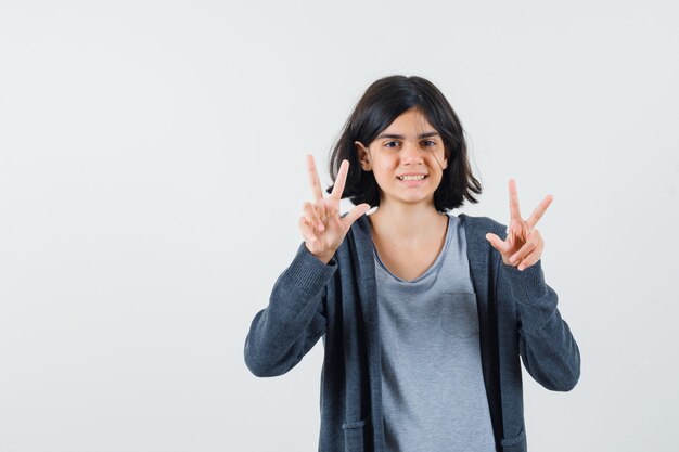 Klein meisje in t-shirt, jasje dat ik hou van je gebaar laat zien en er vrolijk uitziet