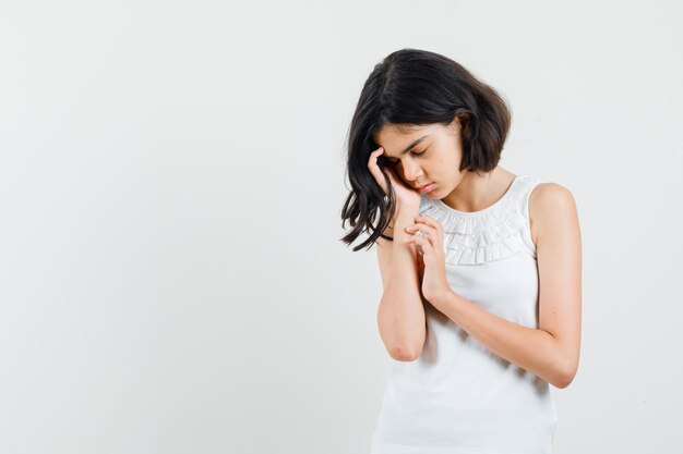 Klein meisje in witte blouse leunend gezicht op palm en op zoek kalm, vooraanzicht.