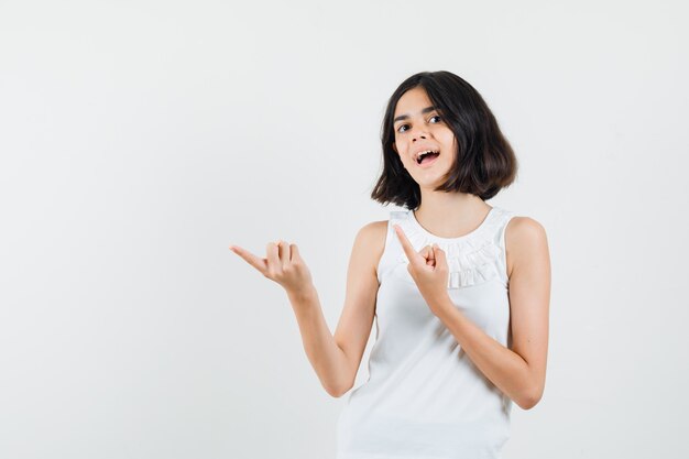 Klein meisje in witte blouse wijzend op de linkerbovenhoek en kijkt vrolijk, vooraanzicht.