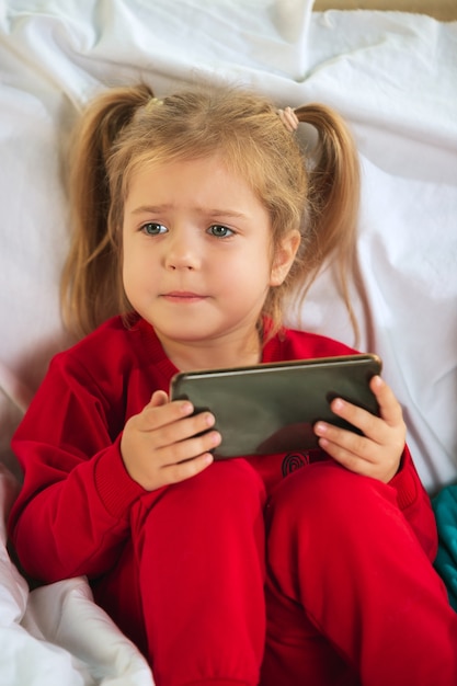 Gratis foto klein meisje in zachte warme pyjama thuis spelen. blanke kinderen in kleurrijke kleding met plezier.