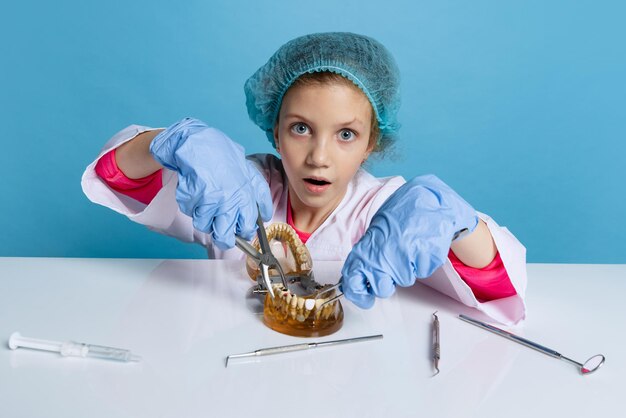 Klein meisje, kind in beeld van tandarts met witte laboratoriumjas en handschoenen geïsoleerd op blauwe achtergrond