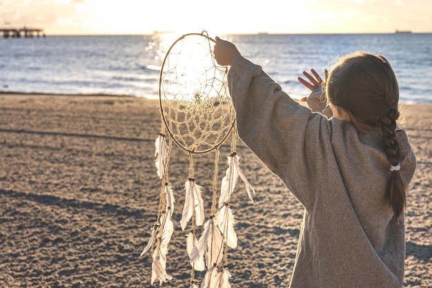 Gratis foto klein meisje met een dromenvanger aan de kust bij zonsondergang