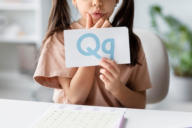 Gratis foto klein meisje met een papier met een letter erop in logopedie