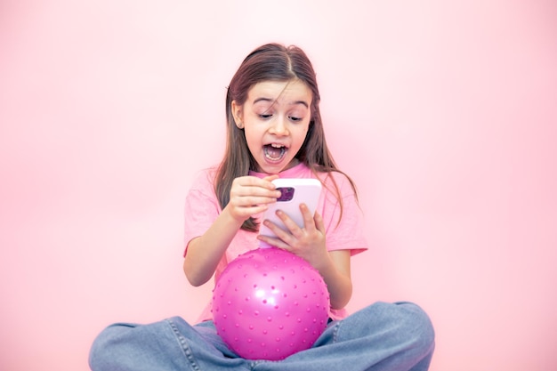 Gratis foto klein meisje met een smartphone in haar handen op een roze achtergrondkopieerruimte