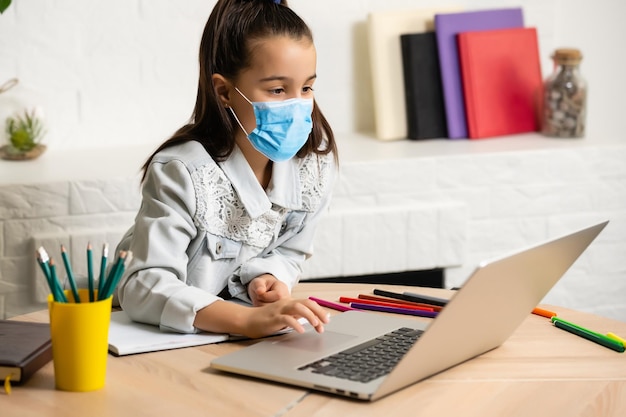 Klein meisje met medisch masker dat thuis studeert. epidemie, pandemie.