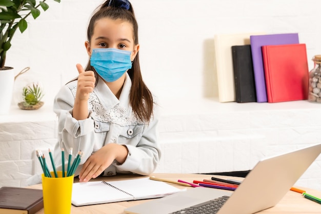 Klein meisje met medisch masker dat thuis studeert. epidemie, pandemie.