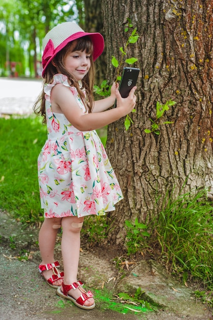 Klein meisje op zoek naar een smartphone terwijl het aanraken van een boom