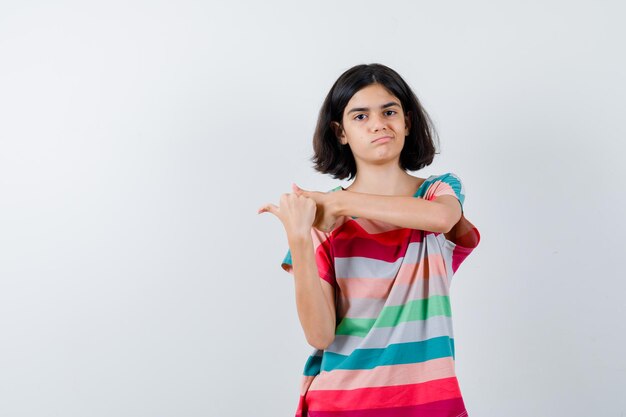 Klein meisje wijst naar links in t-shirt, spijkerbroek en ziet er ontevreden uit. vooraanzicht.