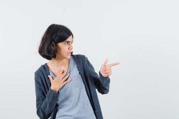 Klein meisje wijst opzij in t-shirt, jasje en kijkt gefocust.