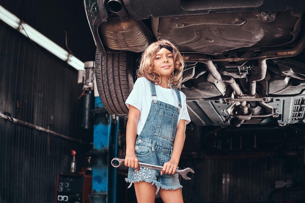 Klein mooi meisje poseert voor fotograaf met gereedschap in autoservicewerkplaats.