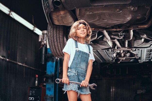 Klein mooi meisje poseert voor fotograaf met gereedschap in autoservicewerkplaats.