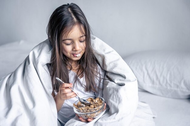 Klein schattig brunette meisje in een wit bed heeft ontbijtgranen