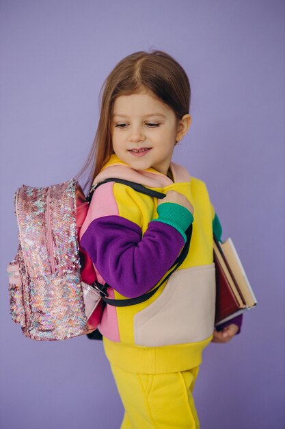 Klein schoolmeisje met boeken en tas geïsoleerd in studio