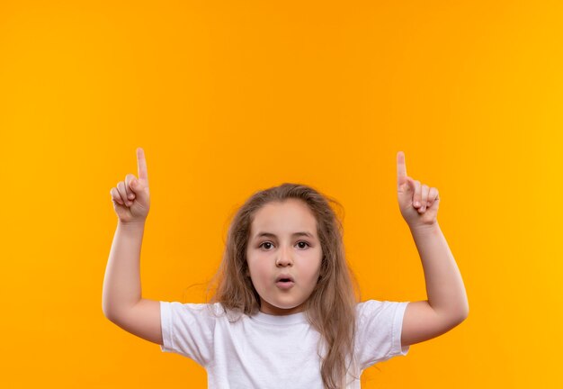 klein schoolmeisje met wit t-shirt stak haar vinger op geïsoleerde oranje muur