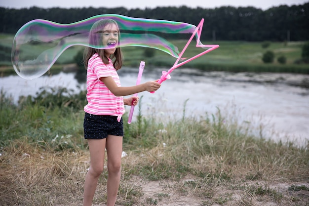 Klein vrolijk meisje speelt met grote zeepbellen in de natuur.