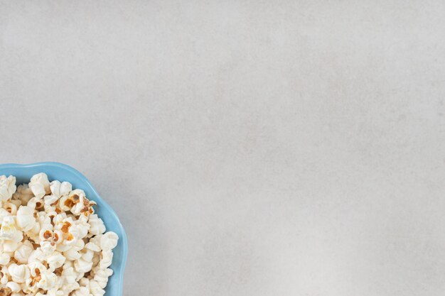 Kleine, blauwe kom gevuld met knapperige popcorn op marmeren tafel.