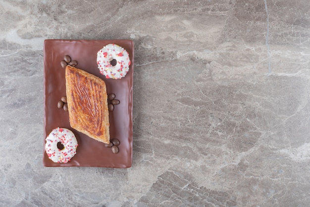 Kleine cake, koffiebonen en hapklare donuts op een schaal op marmeren ondergrond