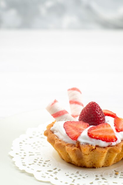kleine cake met room en gesneden aardbeiensuikergoed op wit bureau, fruitcake bessen zoete suiker bak