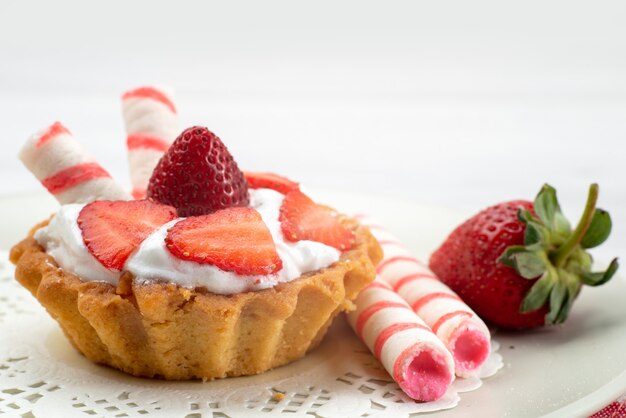 kleine cake met room en gesneden aardbeiensuikergoed op wit bureau, fruitcake bessen zoete suiker