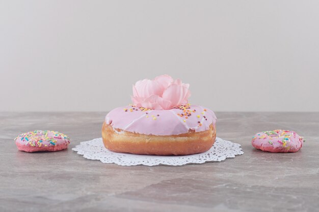 Kleine donuts naast een grote donut versierd met een bloem op marmer