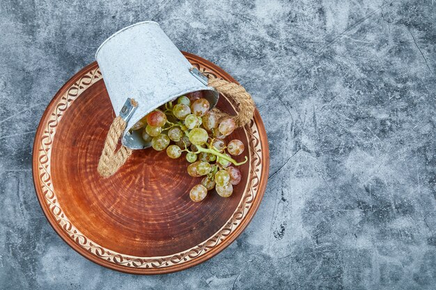 Kleine emmer met druiven in keramische plaat op een marmeren achtergrond.