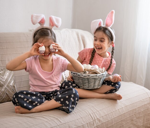 Kleine gelukkige zusjes met konijnenoren poseren met een mandje met paaseieren