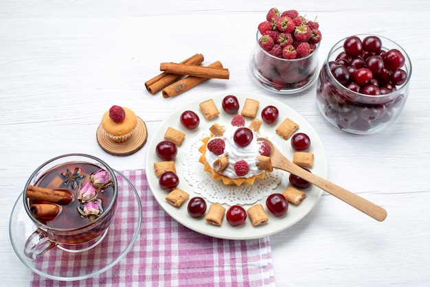 kleine heerlijke cake met frambozen, kersen en kleine koekjes thee kaneel op wit, fruit berry cream tea